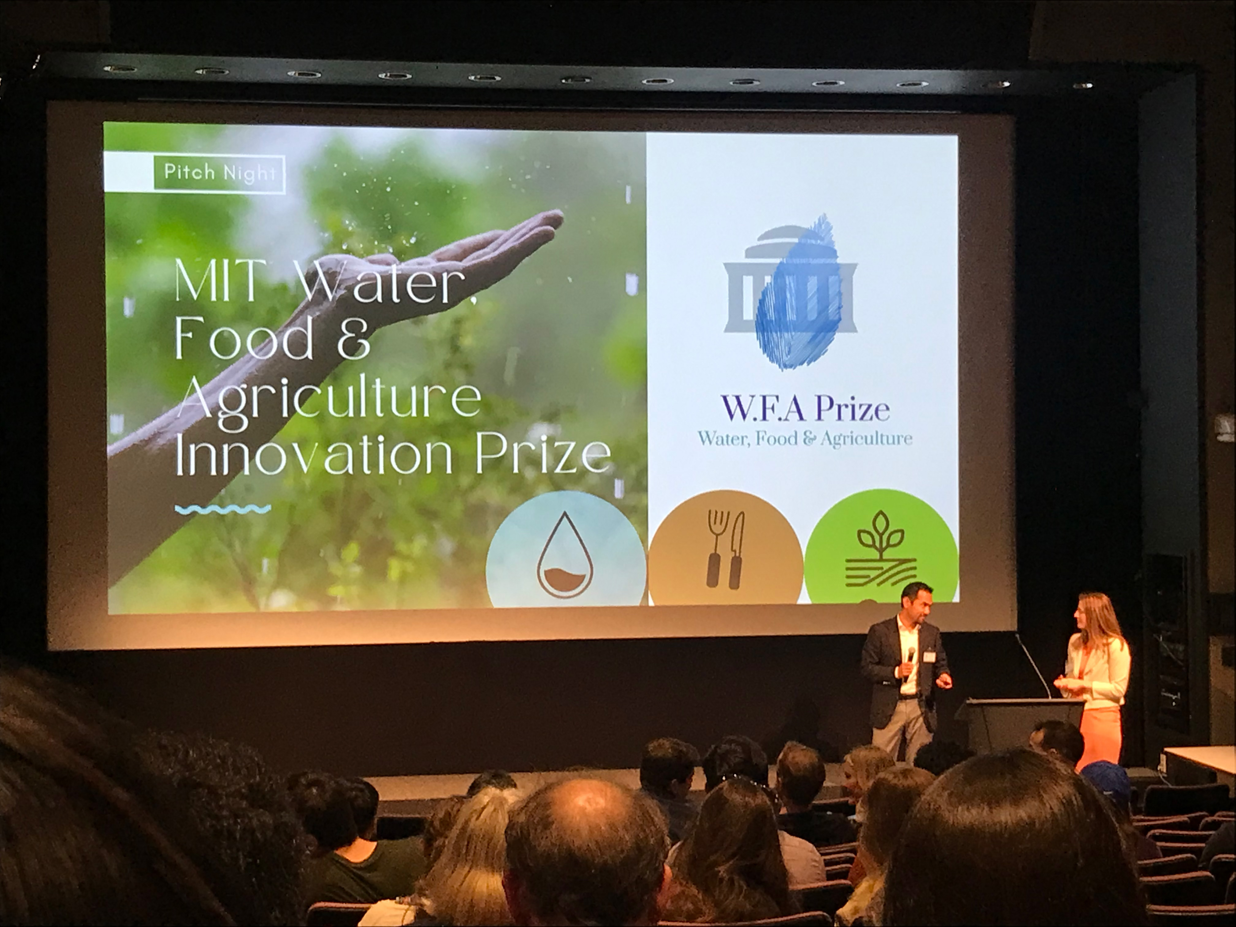 An auditorium full of people watch a presentation with two people at a podium and a slide that says inaugural MIT Water, Food & Agriculture Innovation Prize  