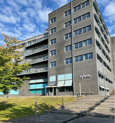 A tall, grey cement office building with light blue accents with a sign that says Xylem on the side