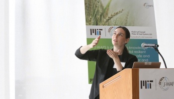 woman presenting at podium with poster behind