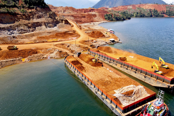 Barges sit along the coast as vehicles load nickel onto them. 