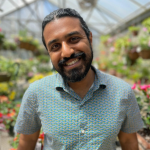 Gokul Sampath, standing inside a green house, with a dark beard 